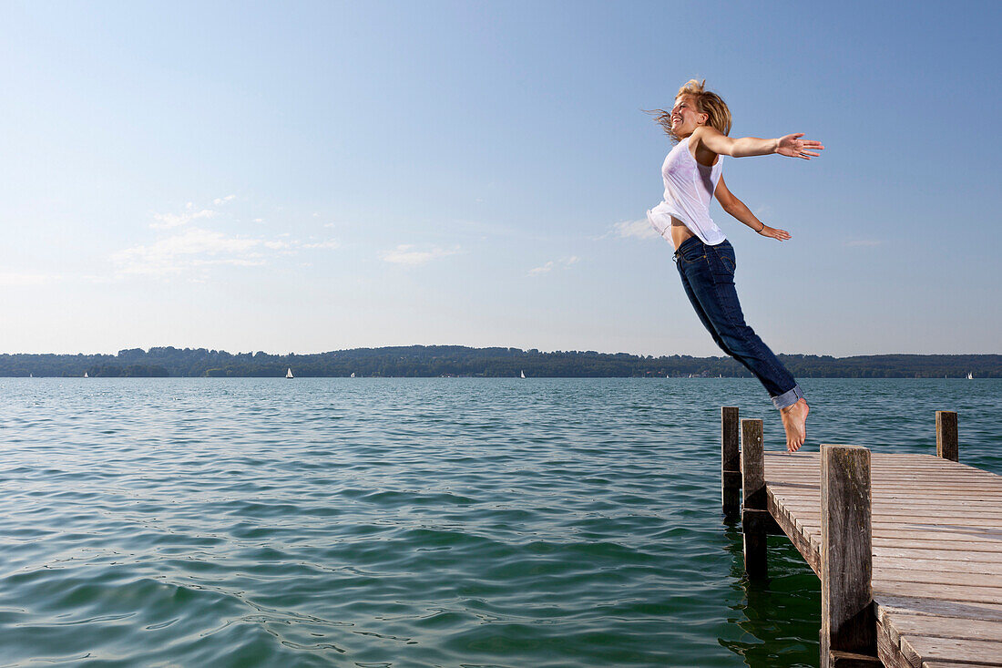Girl jumps from a wooden pier into Lake Starnberg, Bavaria, Germany