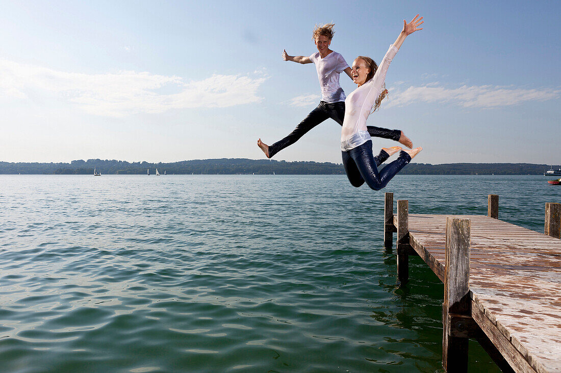 Junges Paar springt von Bootssteg in Starnberger See, Bayern, Deutschland