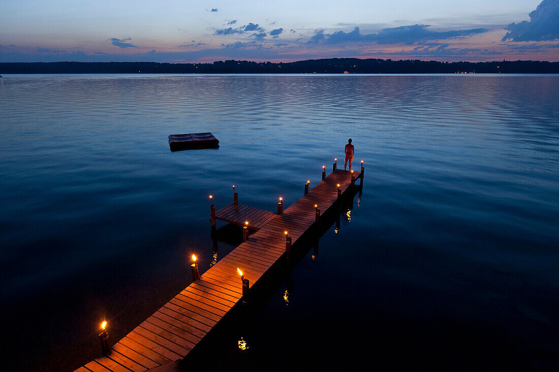 Junger Mann auf Boossteg mit Fackeln in der Abenddämmerung, Starnberger See, Bayern, Deutschland, Europa
