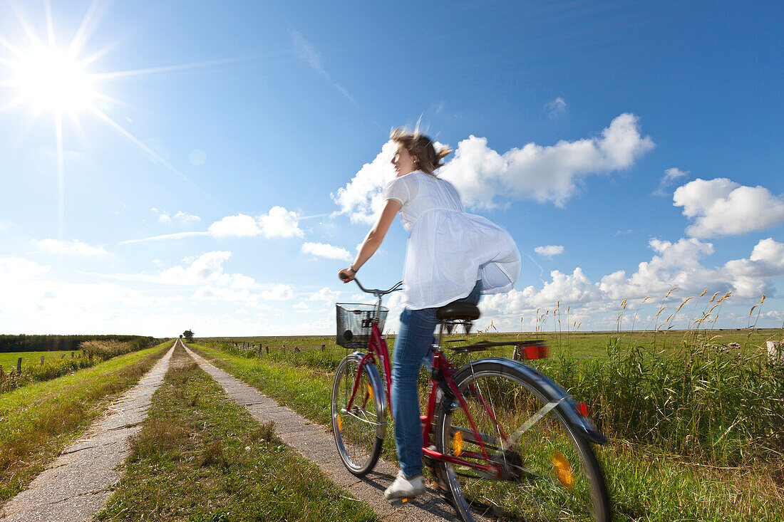 Junge Frau auf Fahrrad in Salzwiesen, Wattenmeer, Nordseeküste, Niedersachsen, Deutschland, Europa