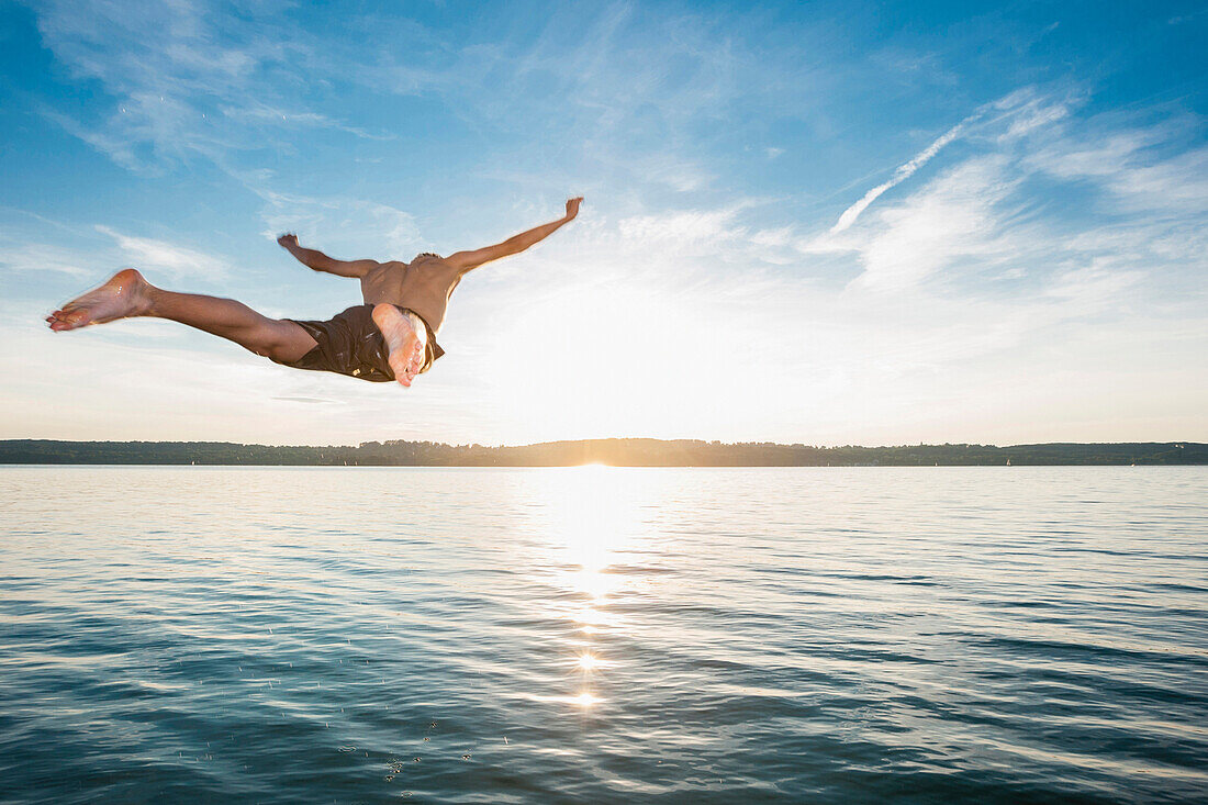 Junger Mann springt in den Starnberger See bei Sonnenuntergang, Oberbayern, Deutschland, Europa