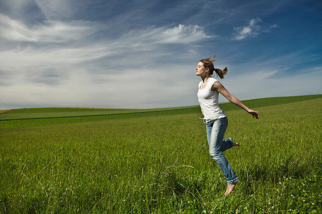 Girl jumping barefoot in a meadow, Upper Bavaria, Germany