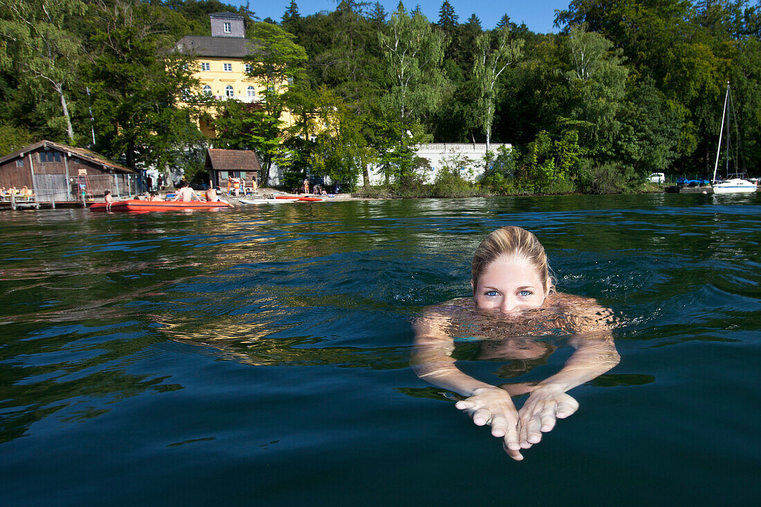 Junge Frau schwimmt in Starnberger See, Schloss Unterallmannshausen im Hintergrund, Oberbayern, Deutschland, Europa