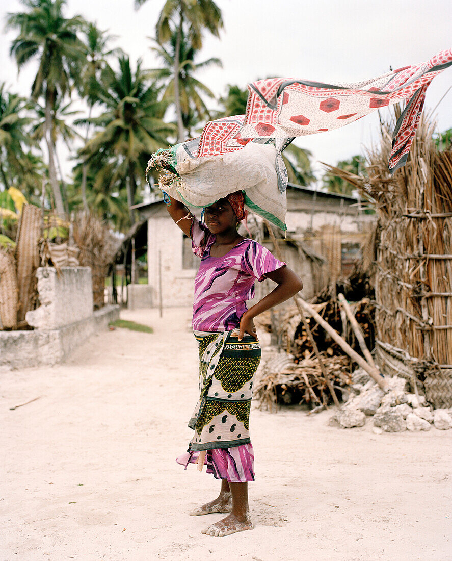Junge Frau in traditioneller Tüchern Kangas, Seetang Ernte tragend, Jambiani, Sansibar, Tansania, Ostafrika