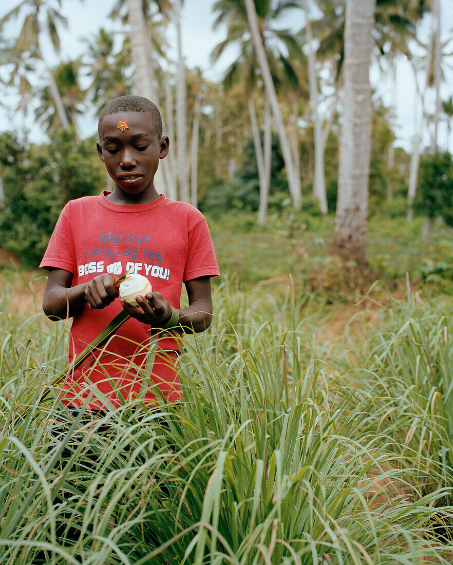 Junge schält Mandarine mit Sternfrucht auf der Stirn, Spice Tour auf der Hakuna Matata Spice Farm im Dorf Dole, bei Kidichi, nordöstlich Zanzibar Town, Sansibar, Tansania, Ostafrika