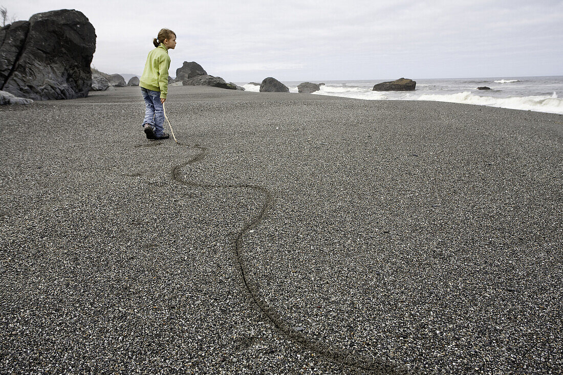 Young Girl Dragging Stick Along Sandy Beach, Redwood National Park, California, USA