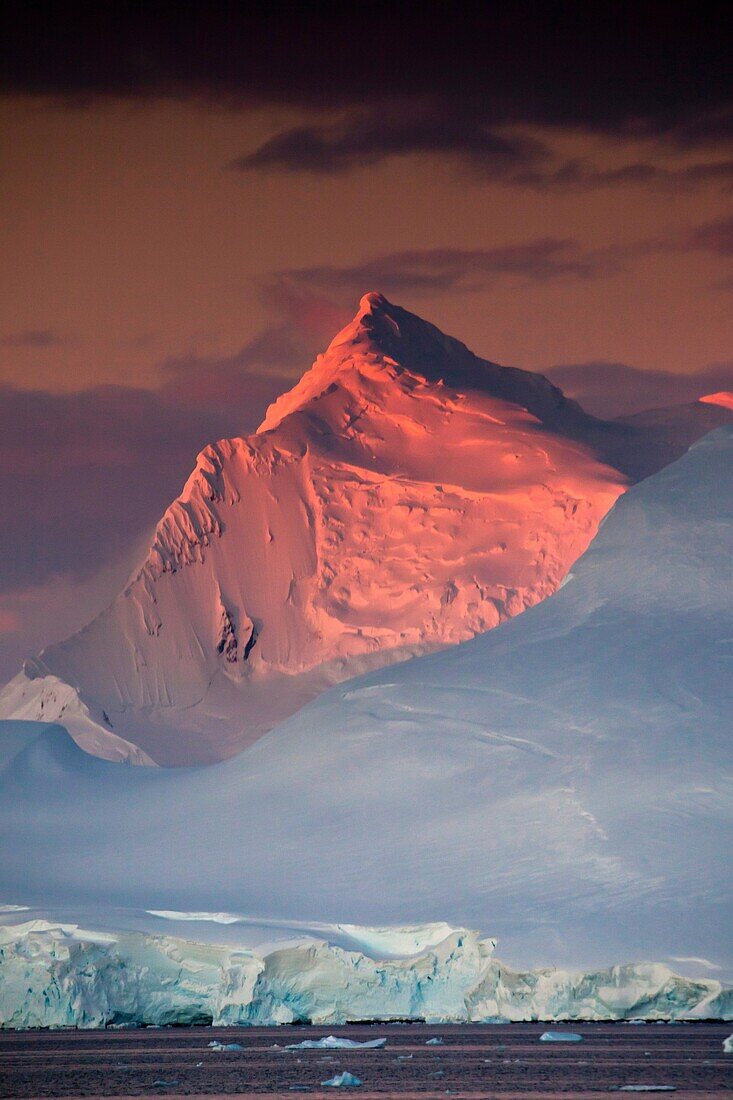 Alpenglow lights up high peaks on Wiencke and Anvers Islands behind Port Lockroy, Antarctic Peninsula