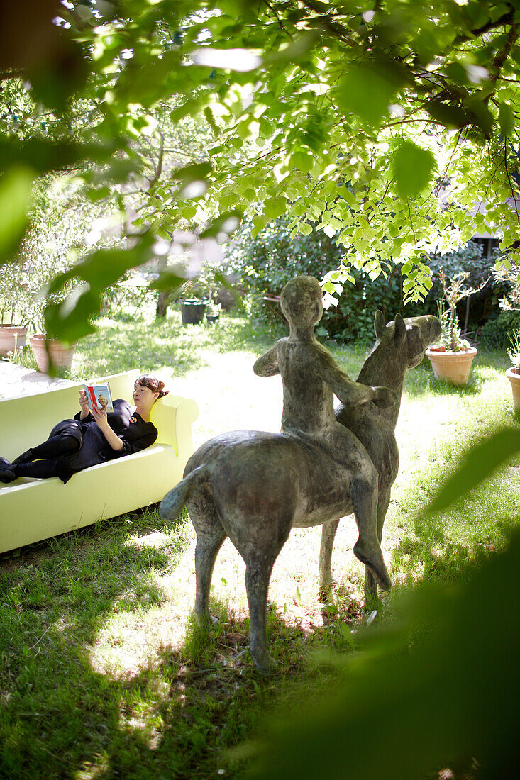 Frau liest auf der Couch im Garten mit Skulptur, B und B Chambre Avec Vue, Luberon, Frankreich