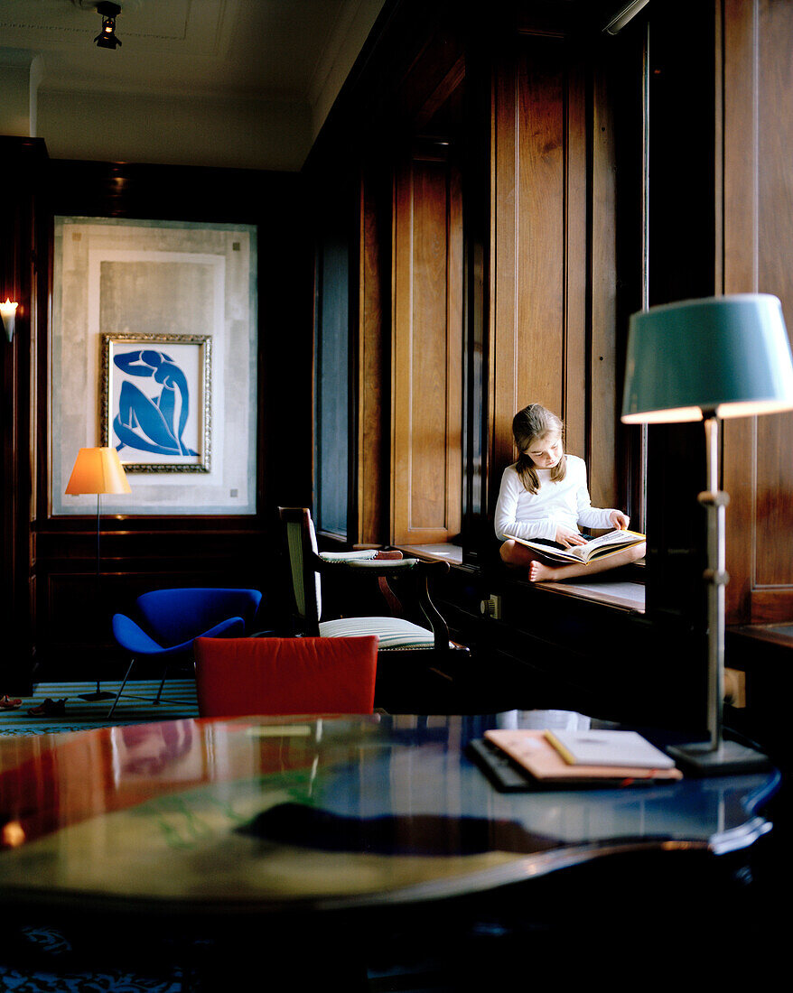 Girl reading a book while sitting on a window sill in a hotel room, Rotterdam, Netherlands