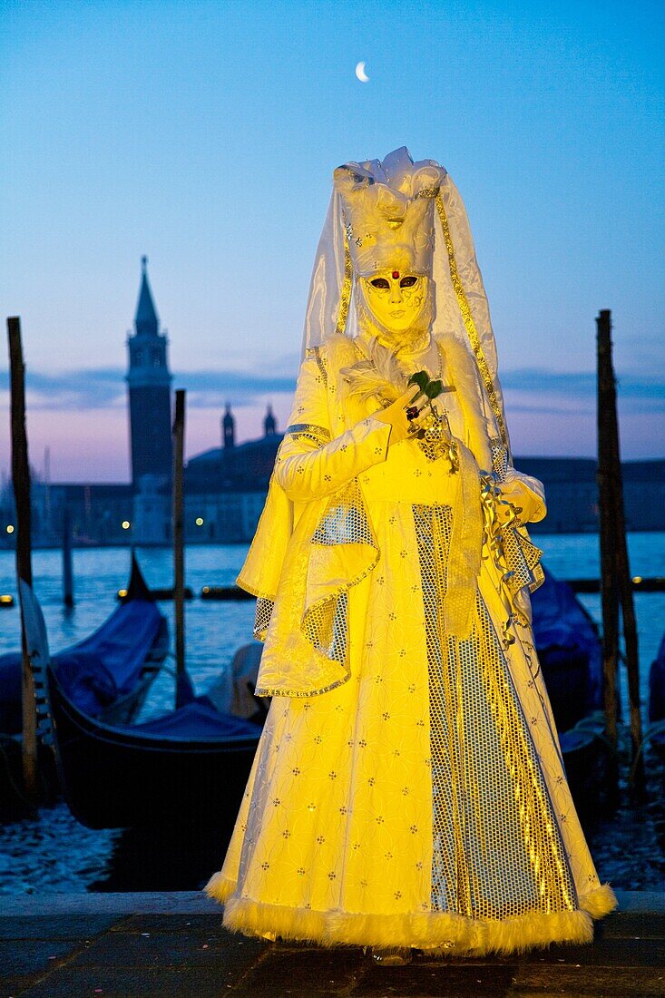 A masked woman in front of gondolas at dawn at the carnival in Venice, Italy, Europe