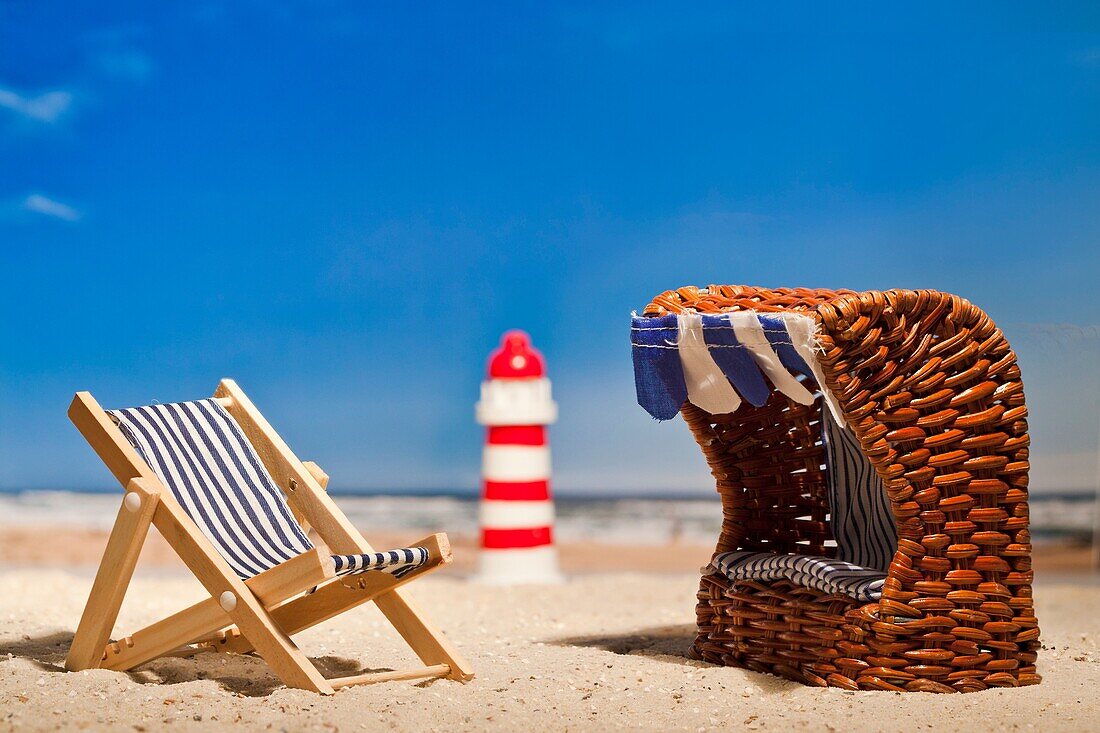 Still life of a miniature lighthouse, deck chair and roofed wicker beach chair