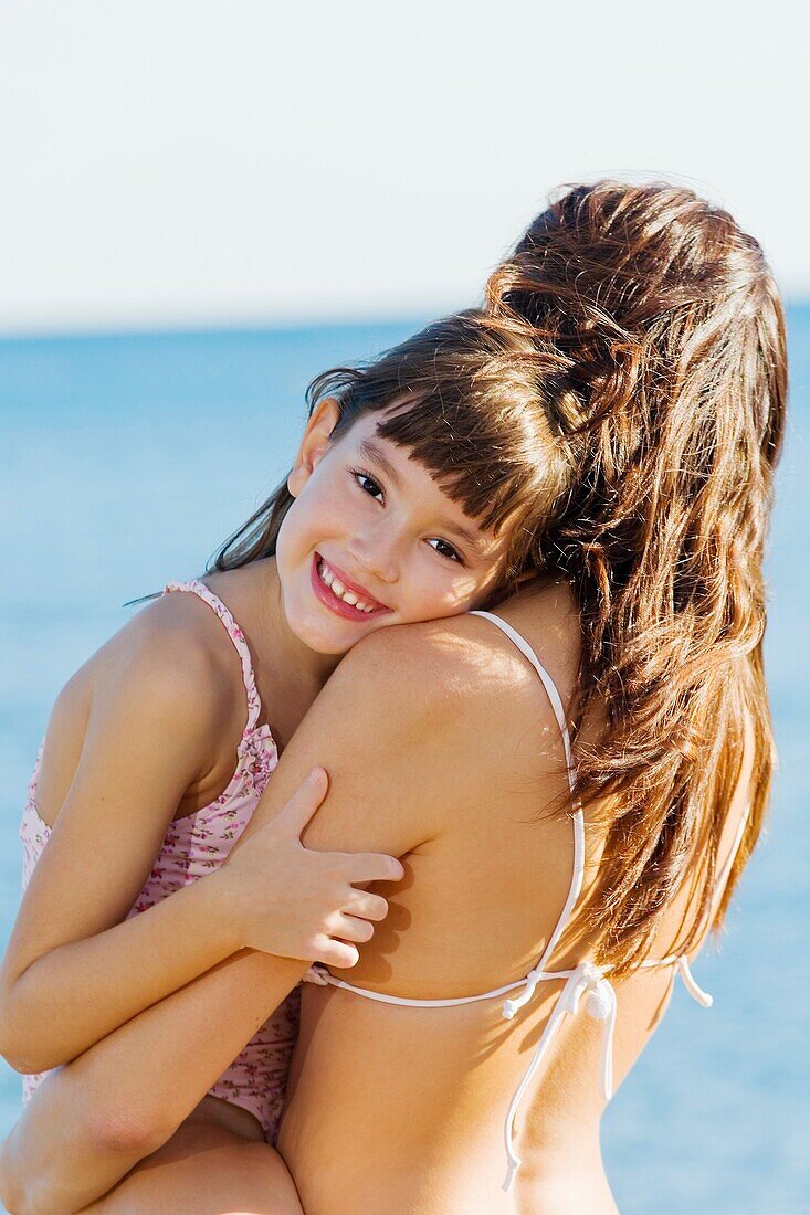 Daughter giving a hug to her mother and looking at camera in the seashore