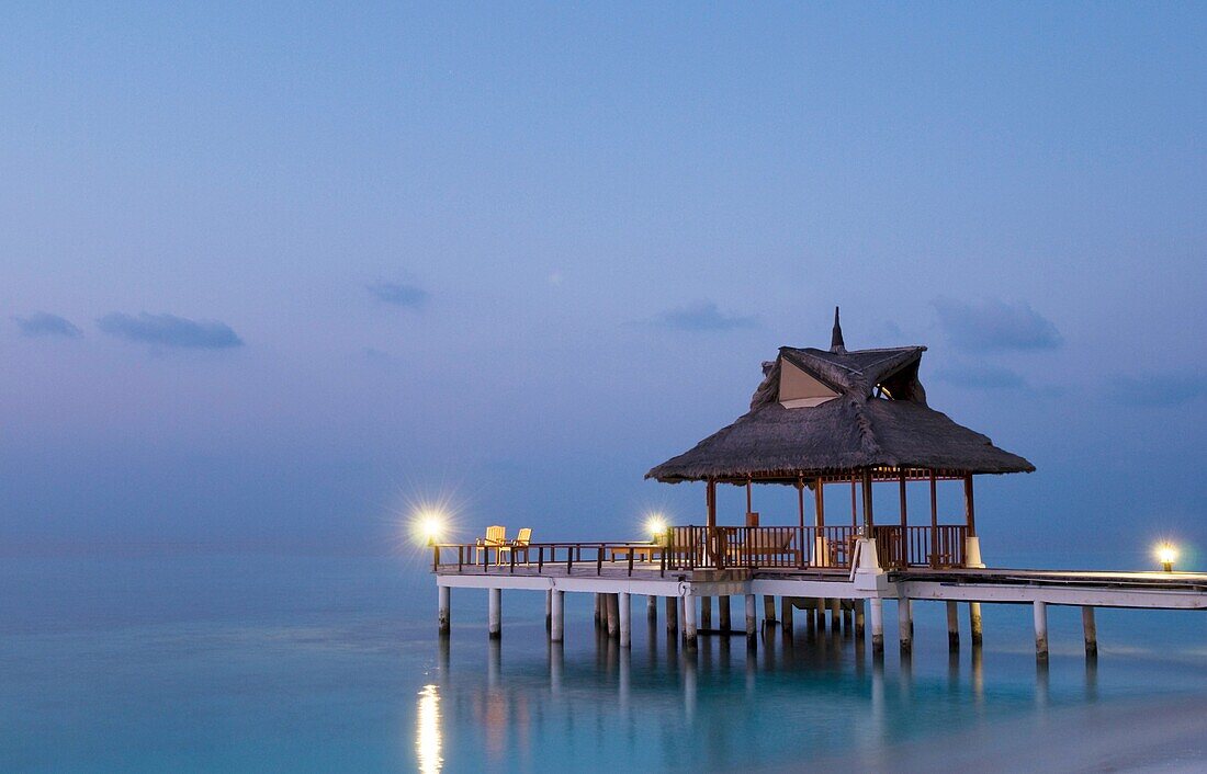 Gazebo and jetty with straw roof at a resort in the Maldives at dusk