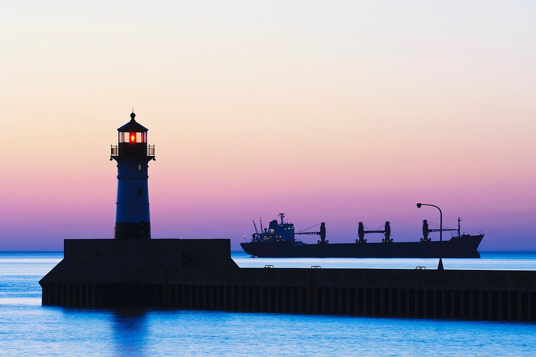 A ship awaits entry to Duluth Harbor with the north breakwater light silhouetted against the glow of the sunrise