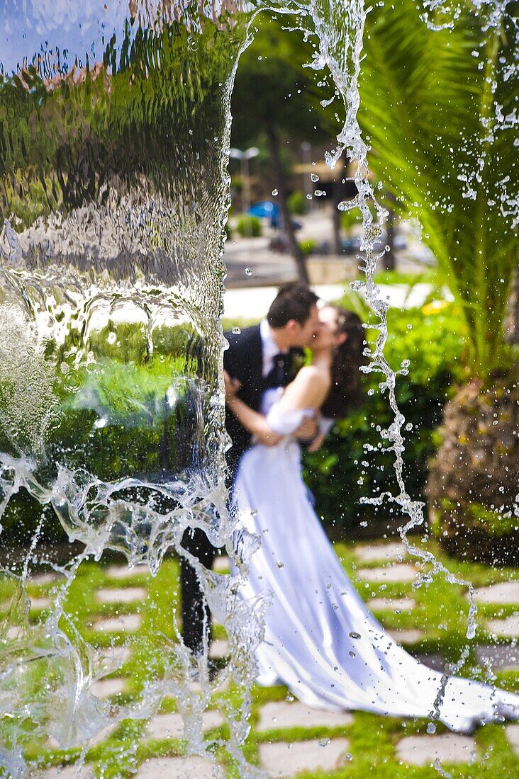 Bride and groom kissing behind a water cascade