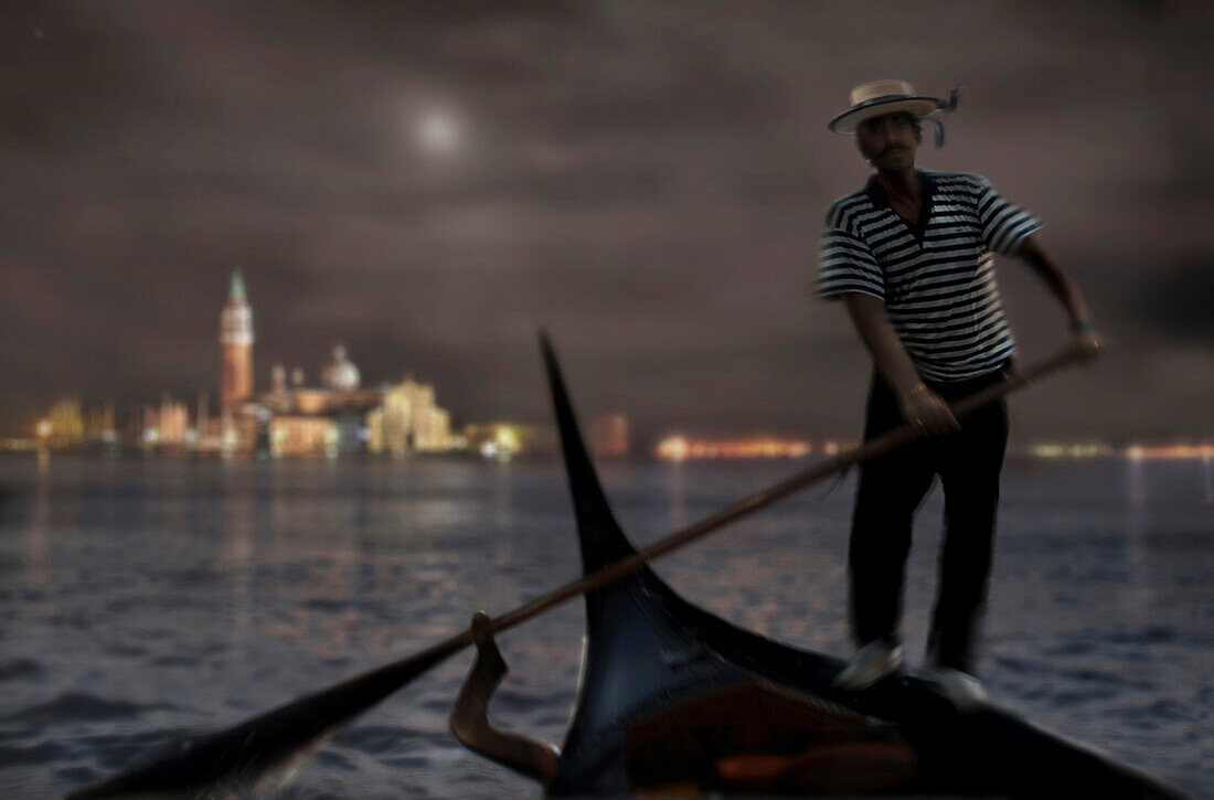 Gondelführer mit Gondel in der Nacht und Stadtansicht im Hintergrund, Venedig, Italien