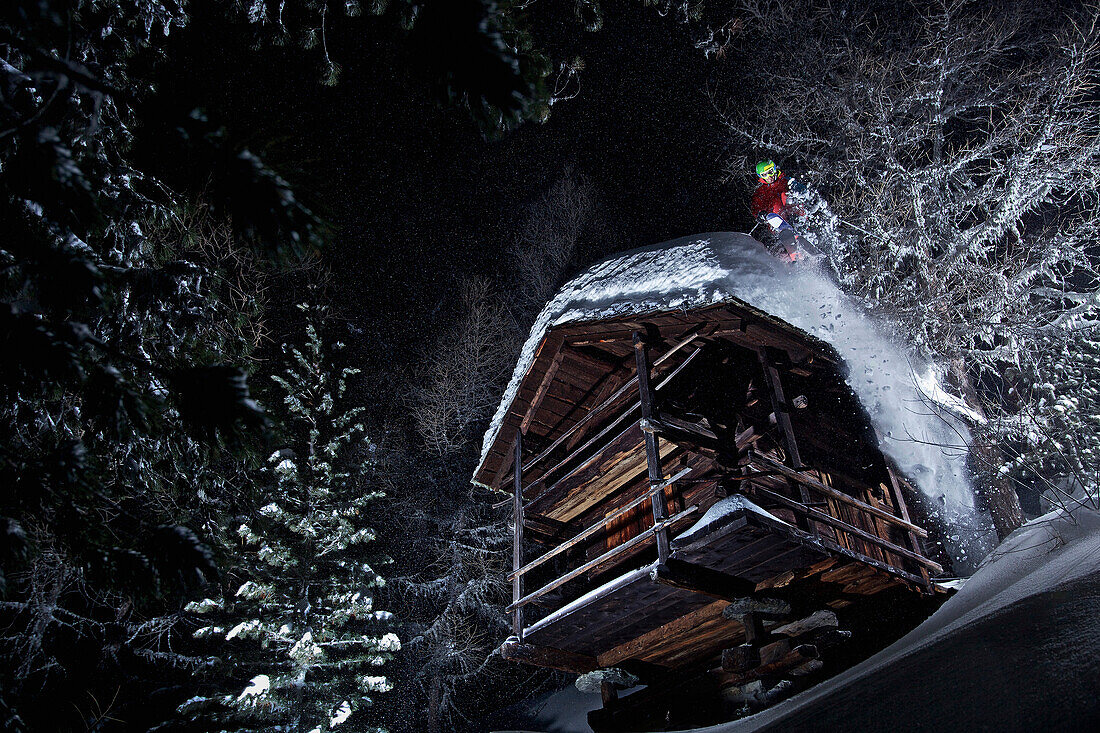 Junger Skifahrer springt von einer kleinen Holzhütte herunter bei Dunkelheit, Chandolin, Wallis, Schweiz, Europa