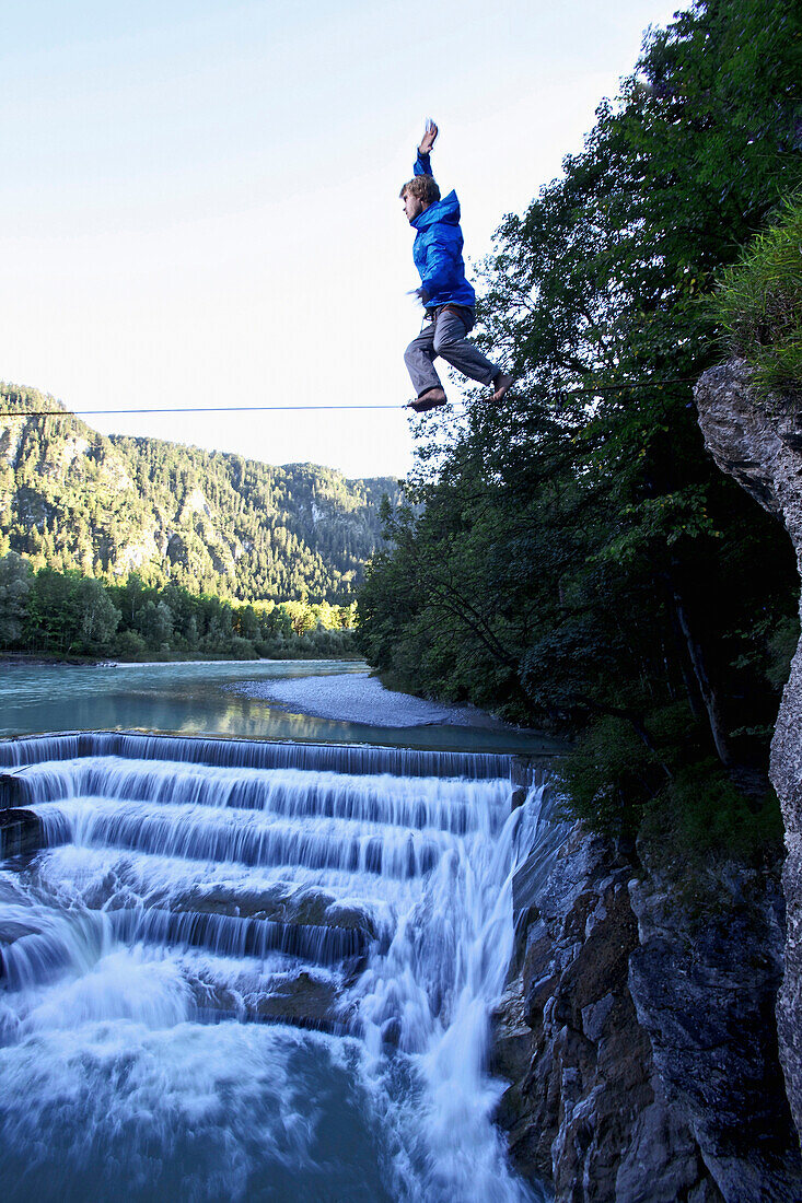 Young man balancing on a highline over a stream, Fuessen, Bavaria, Germany, Europe