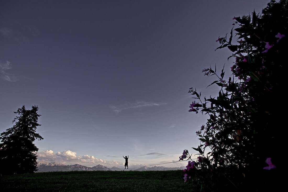 Junger Mann balanciert über eine Longline in der Abenddämmerung, Auerberg, Bayern, Deutschland, Europa
