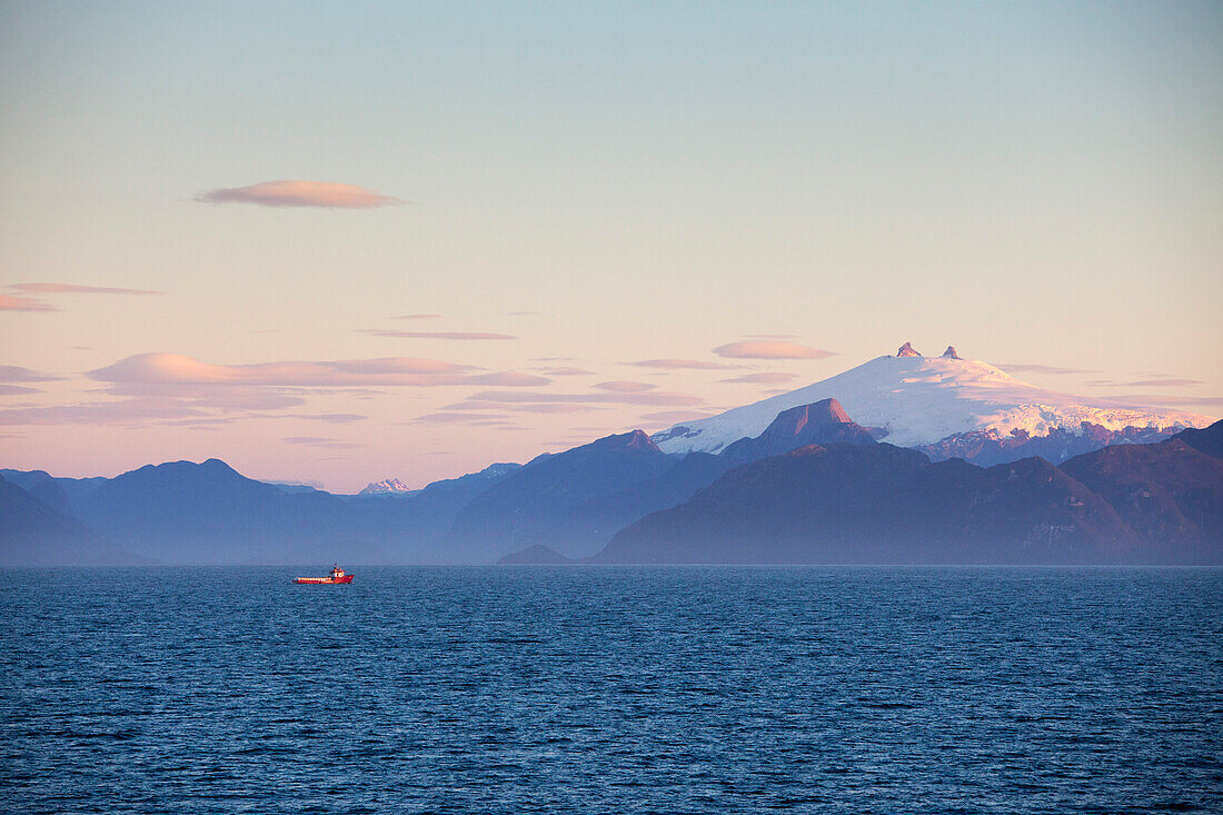Fischerboot und schneebedeckter Vulkan, Chilenische Fjorde in der Abenddämmerung, Magallanes y de la Antartica Chilena, Patagonien, Chile, Südamerika