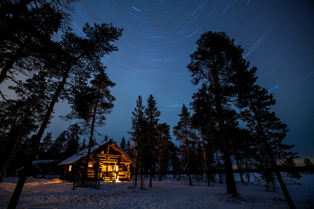 Blockhütte und Sternenbahnen am See Nangujärvi bei Nacht, Lappland, Finnland, Europa