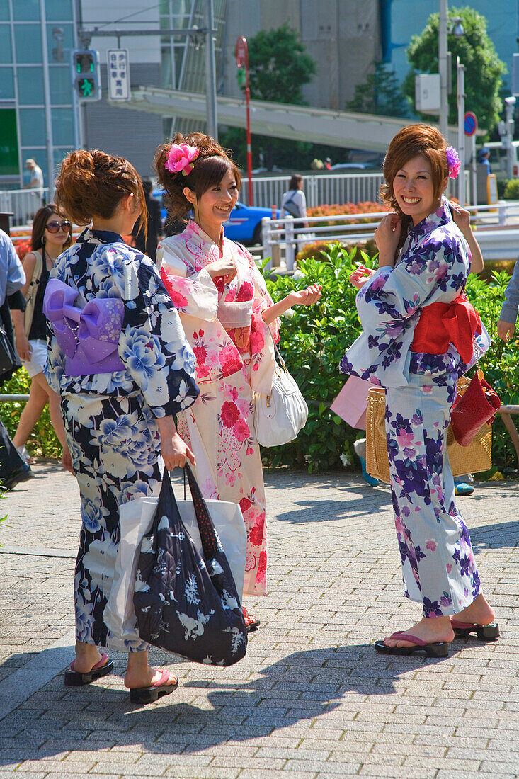 Three young Japanese women in yukata summer kimono stroll in the Roppongi District of central Tokyo, Japan.