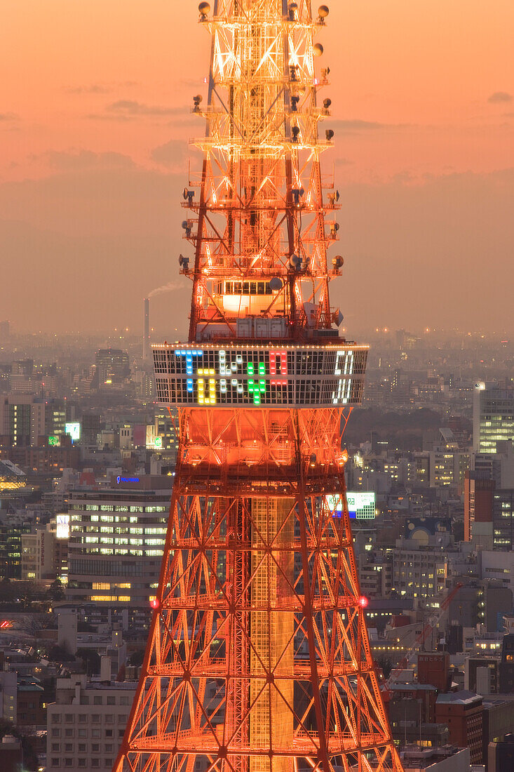 A telephoto view emphasizes the elegant orange-colored steel girder construction of Tokyo Tower against a twilight sky and city lights in central Tokyo, Japan.