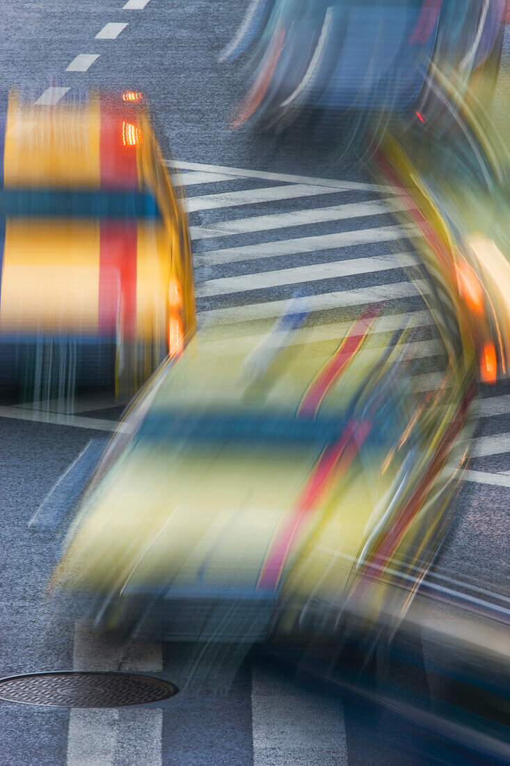 A slow shutter speed blurs colorful taxis at the scramble crossing in front of Shibuya Station, located in the Shibuya District of Tokyo, Japan.