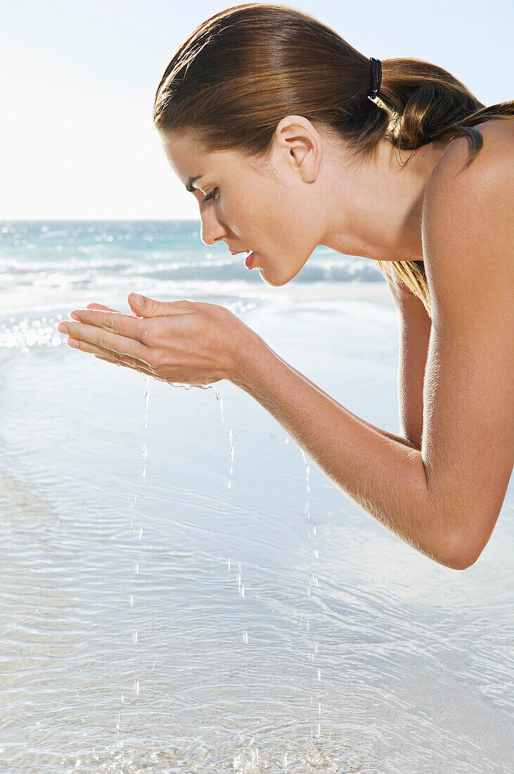 A female washing her face. A portrait shot of a female washing her face in sea water, with the sea in the background.