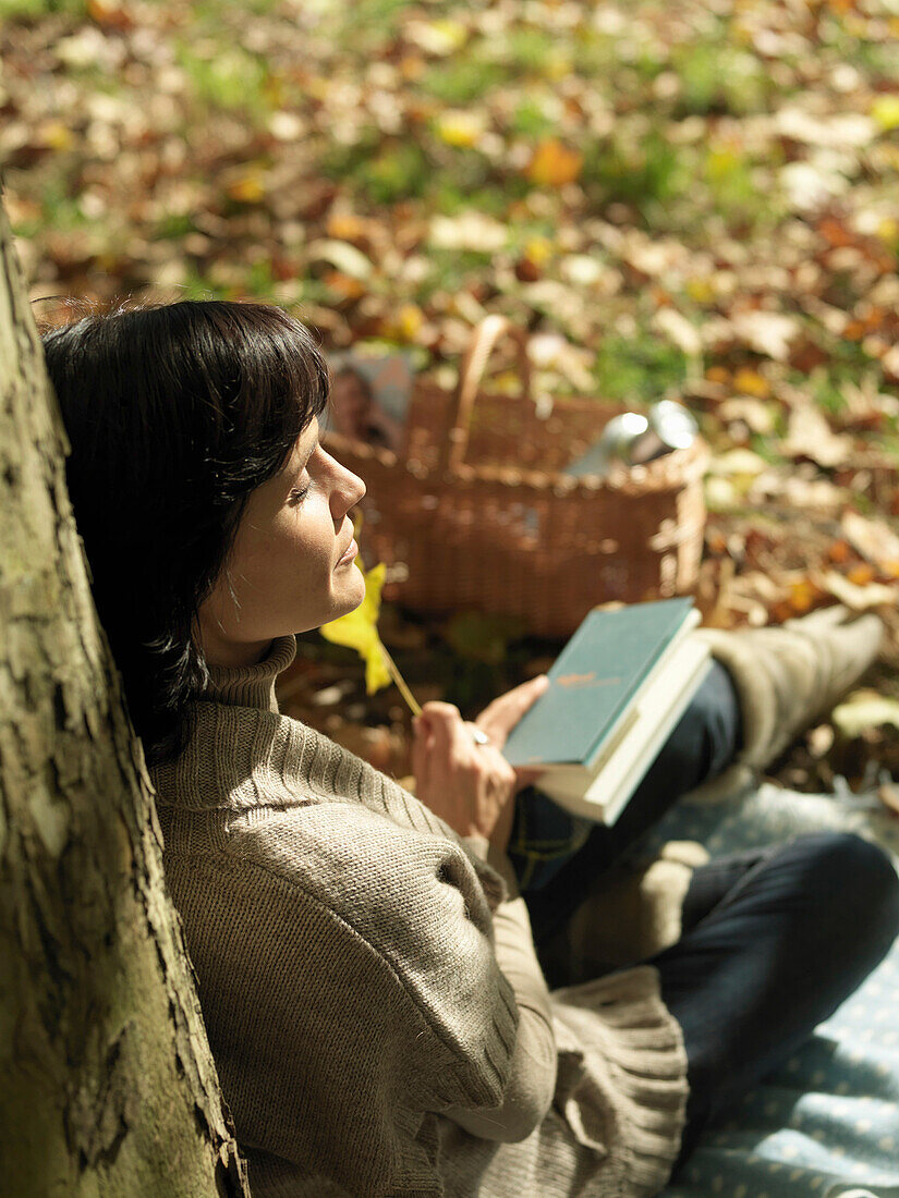 Woman reading under tree in Autumn