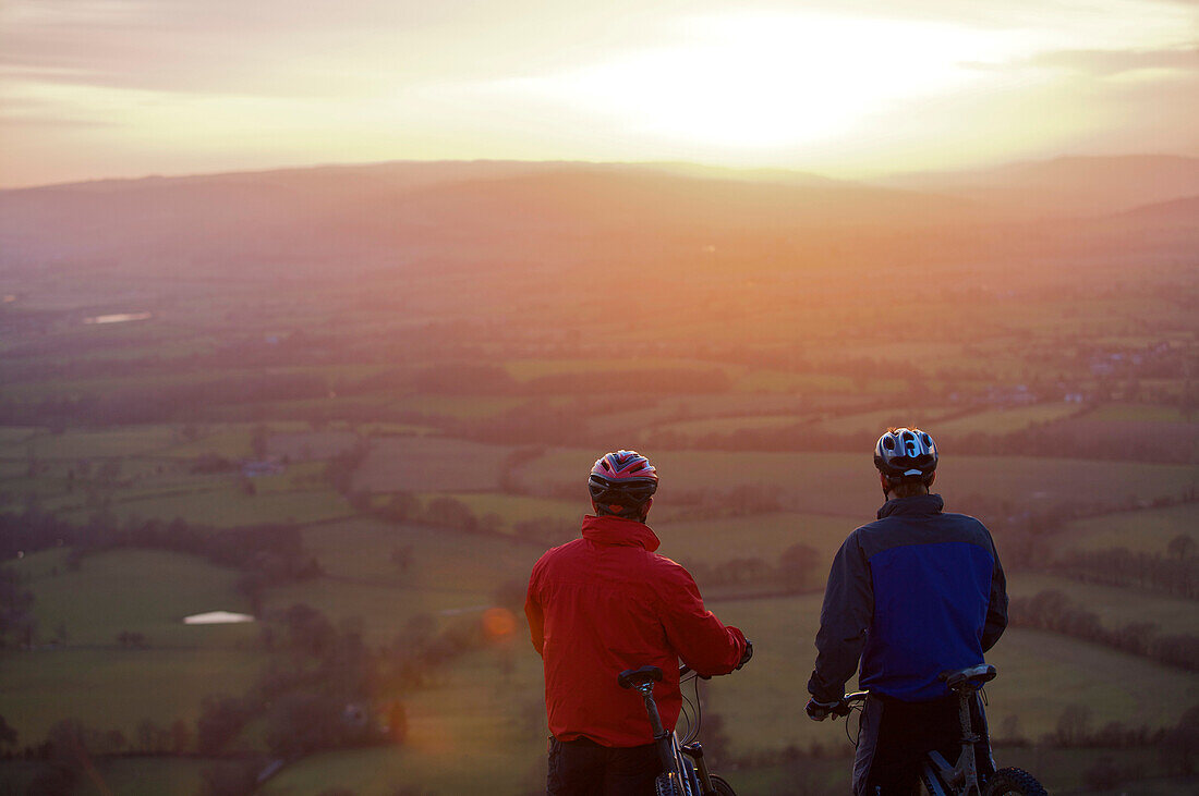 Two mountain bikers viewing scene. View of two mountain bikers standing together looking at a sunset.