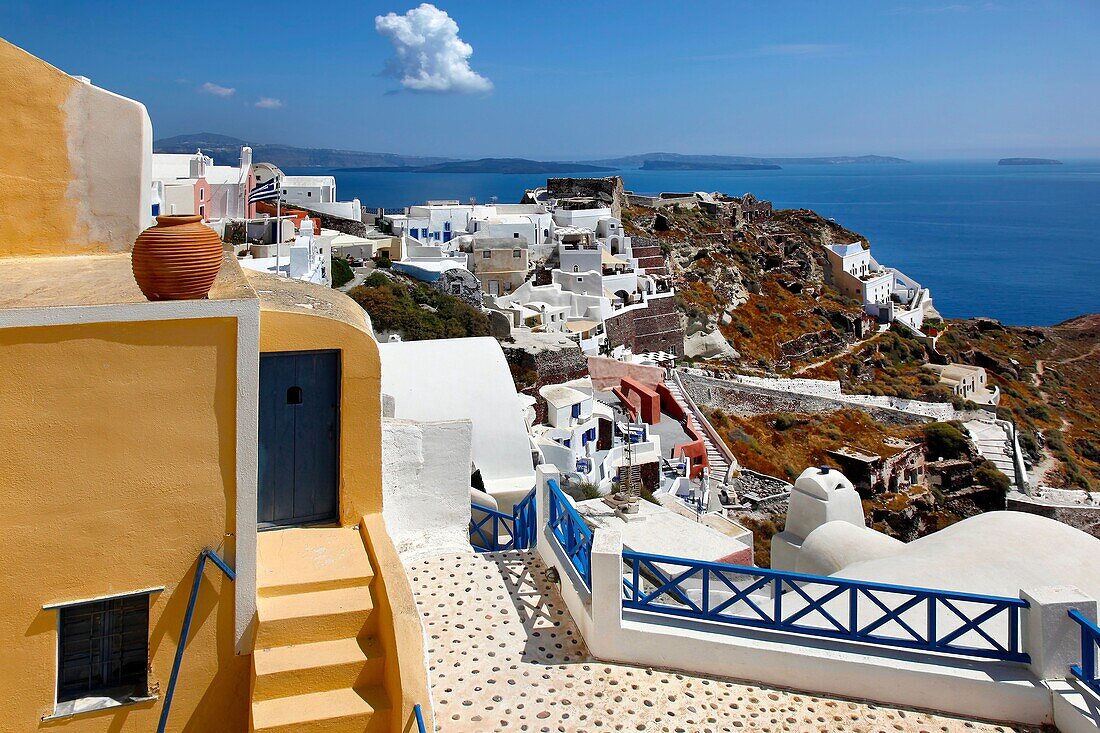 Yellow home with blue fencing and deck overlooking hillside and caldera in the village of Oia in Santorini, Greece