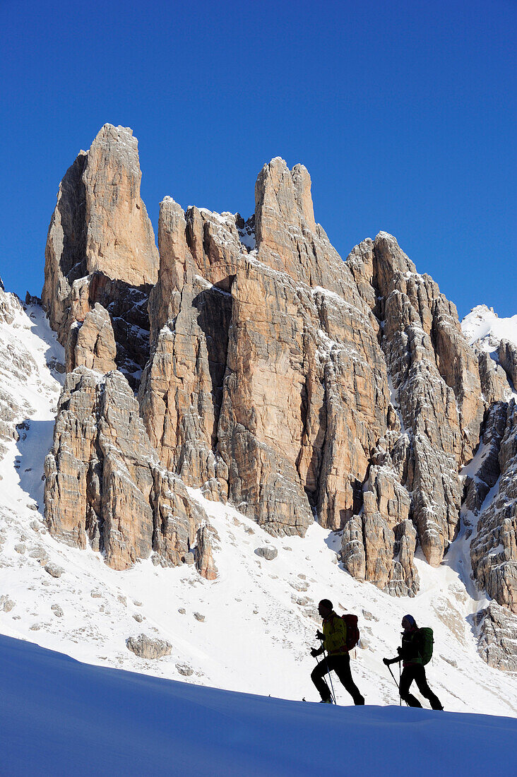 Young woman and young man ascending with crosscountry skis to Corno d'Angolo, rock faces in background, Corno d'Angolo, Cortina, Veneto, Dolomites, Italy, Europe