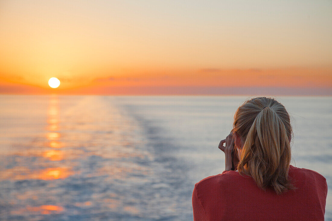 Eine junge Frau fotografiert den Sonnenuntergang von an Bord Kreuzfahrtschiff MS Deutschland (Reederei Peter Deilmann), nahe Kaimaninseln (Cayman-Inseln), Karibik