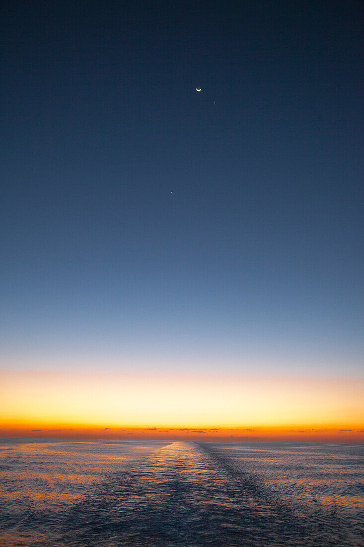 Horizont im Dämmerlicht mit Mond, Planeten und Welle hinterm Kiel von Kreuzfahrtschiff MS Deutschland (Reederei Peter Deilmann), nahe Kaimaninseln (Cayman-Inseln), Karibik