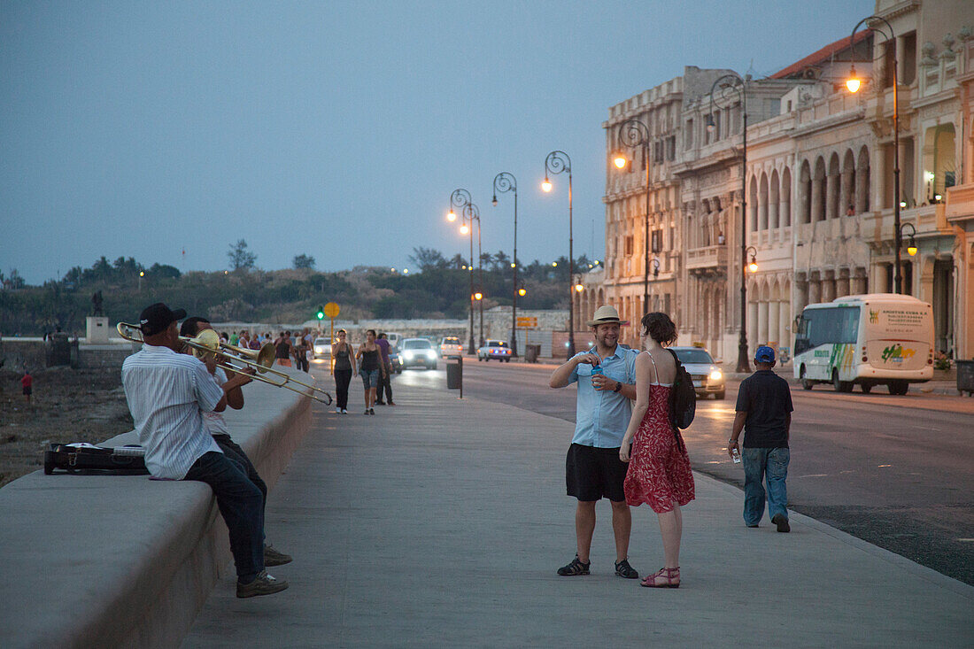 Street musicians performing on Malecon sea drive as tourists pass by at dusk, Havana, Havana, Cuba, Caribbean