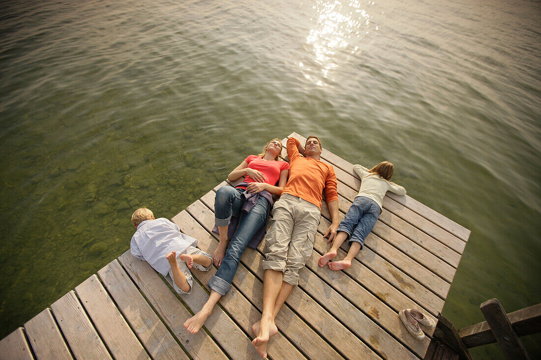 Familie mit Kindern liegt auf einem Steg am See, Wörthsee, Oberbayern, Bayern, Deutschland