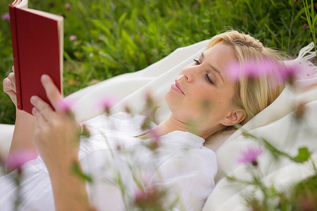 Junge Frau liegt lesend auf einer Wiese
