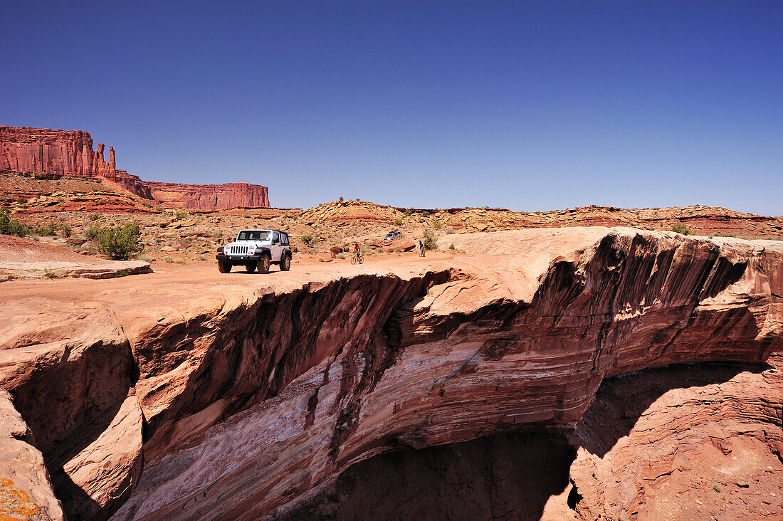 Jeep fährt an Felsabbruch über Colorado River entlang, White Rim Drive, White Rim Trail, Island in the Sky, Canyonlands Nationalpark, Moab, Utah, Südwesten, USA, Amerika