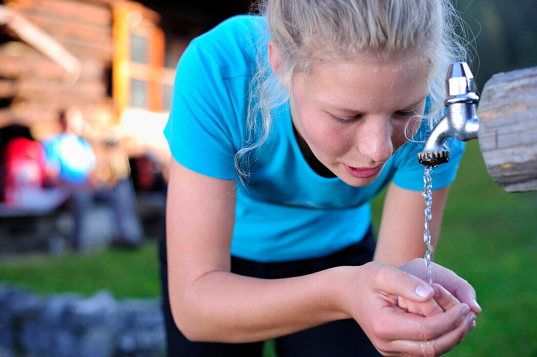 Junge Frau trinkt Wasser aus einem Brunnen, Unnütz, Brandenberger Alpen, Tirol, Österreich