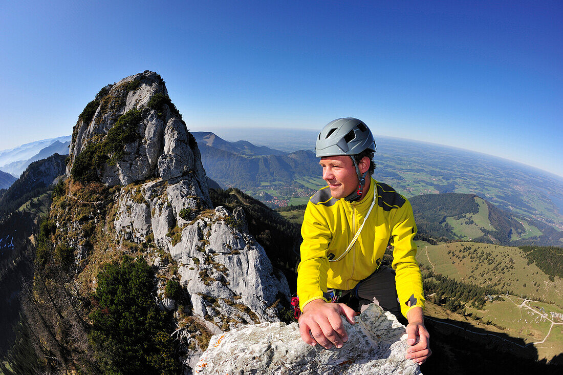 Junger Mann erreicht Spitze eines Felsturms, Kampenwand, Chiemgauer Alpen, Chiemgau, Oberbayern, Bayern, Deutschland
