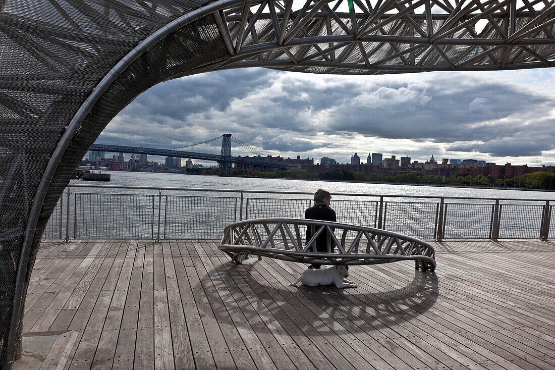 New York - United States, the Williamsburg bridge and the skyline of Manhattan view from the North piers a new real estate project on the East river, woman sitting on a bench