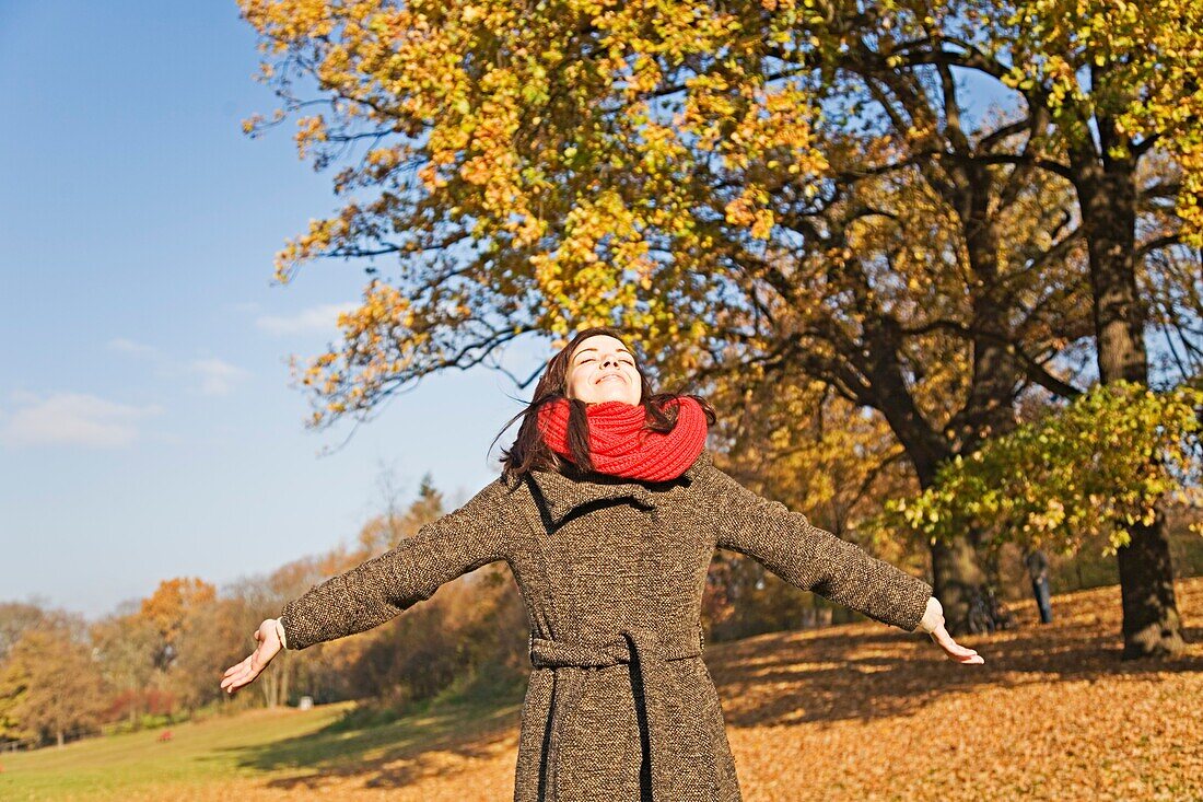 Portrait of a brunette woman in park in Autumn with arms opened