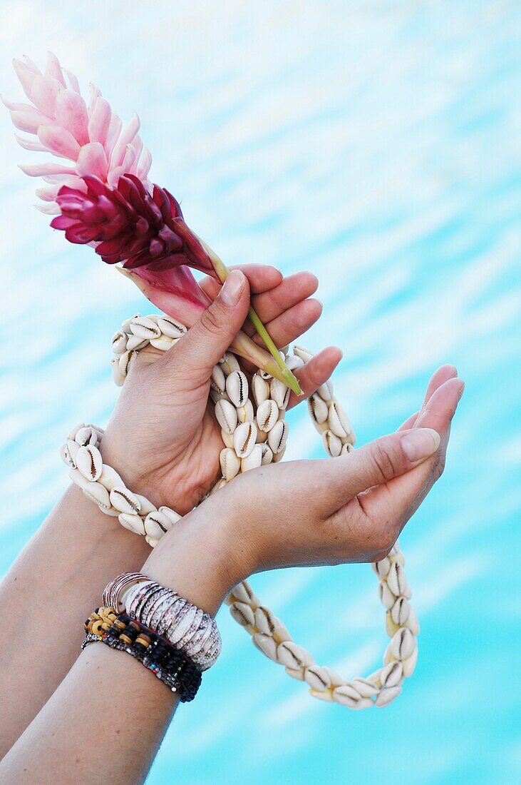 Close-up of woman's hands holding flowers and sea shell necklace