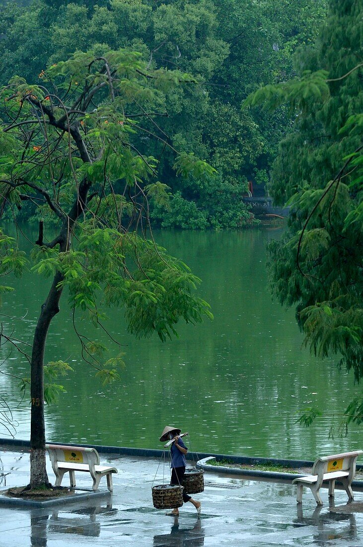 Asia, Southeast Asia, Vietnam, Hanoi, Lake Hoan Kiem, woman carrying a yoke along the lake