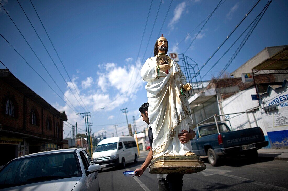 A man holds a sculpture of Saint Jude Thaddeus as he asks for charity in a street of Mexico City, February 15, 2010