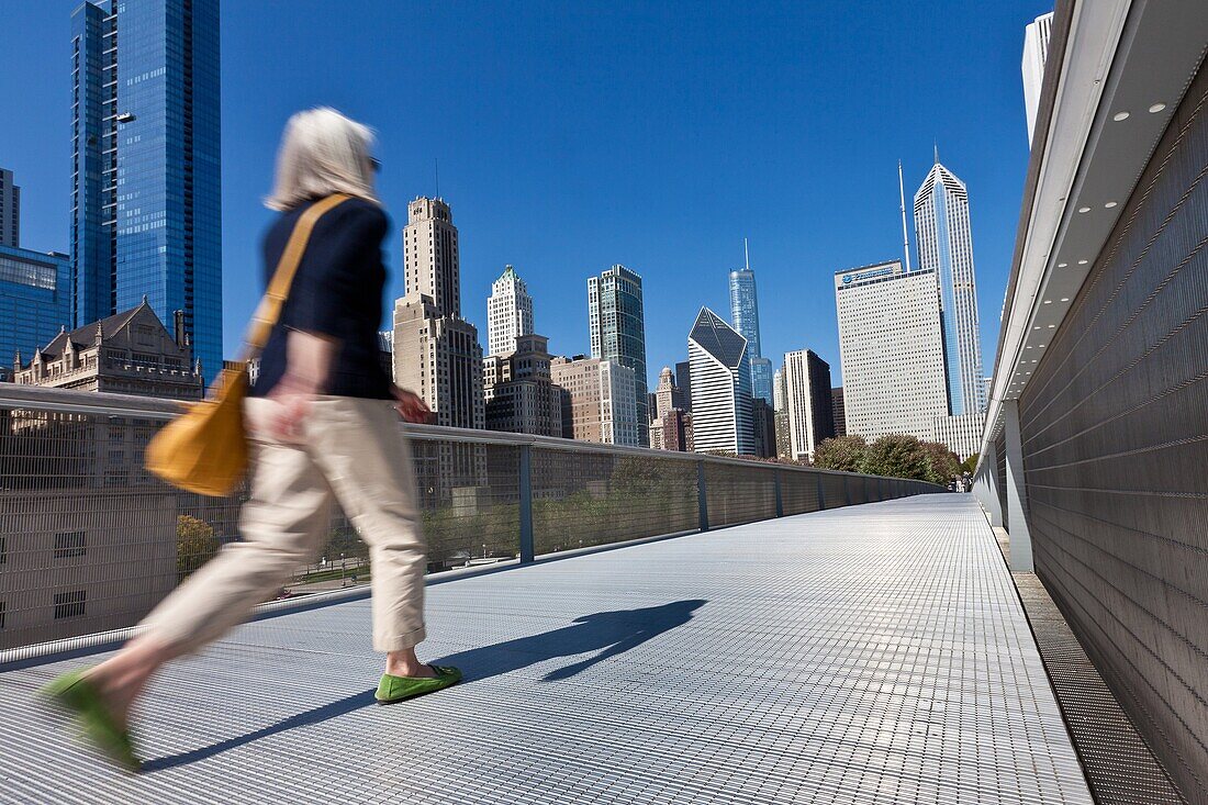 A pedestrian walks the Nichols Bridgeway with the Skyline of Chicago from Millennium Park in Chicago, IL, USA