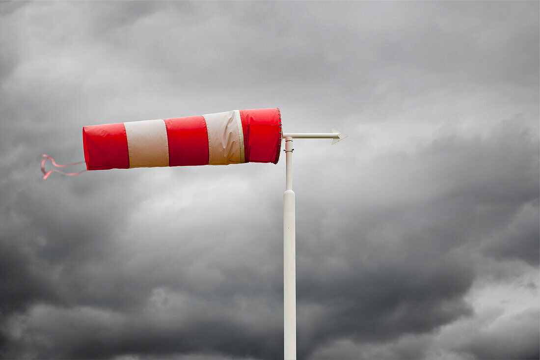 Red and white wind vane. Wind sock, weather indicator at an airfield.  Windblown, at vertical level in stormy weather. Indicating the wind direction. Dark storm clouds in the sky., Wind Vane in stormy weather