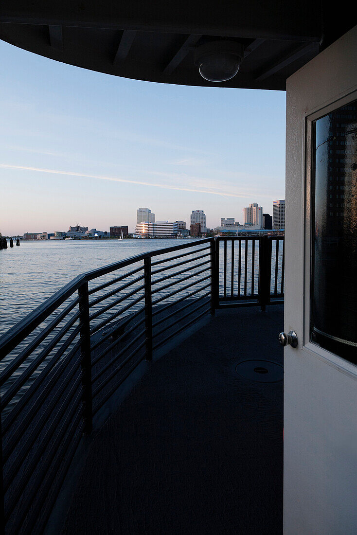 View from the deck on the ferry from Portsmouth across the Elizabeth River, Norfolk, Virginia. View of the Norfolk skyline buildings, and the river at sunset., Norfolk, Virginia, USA