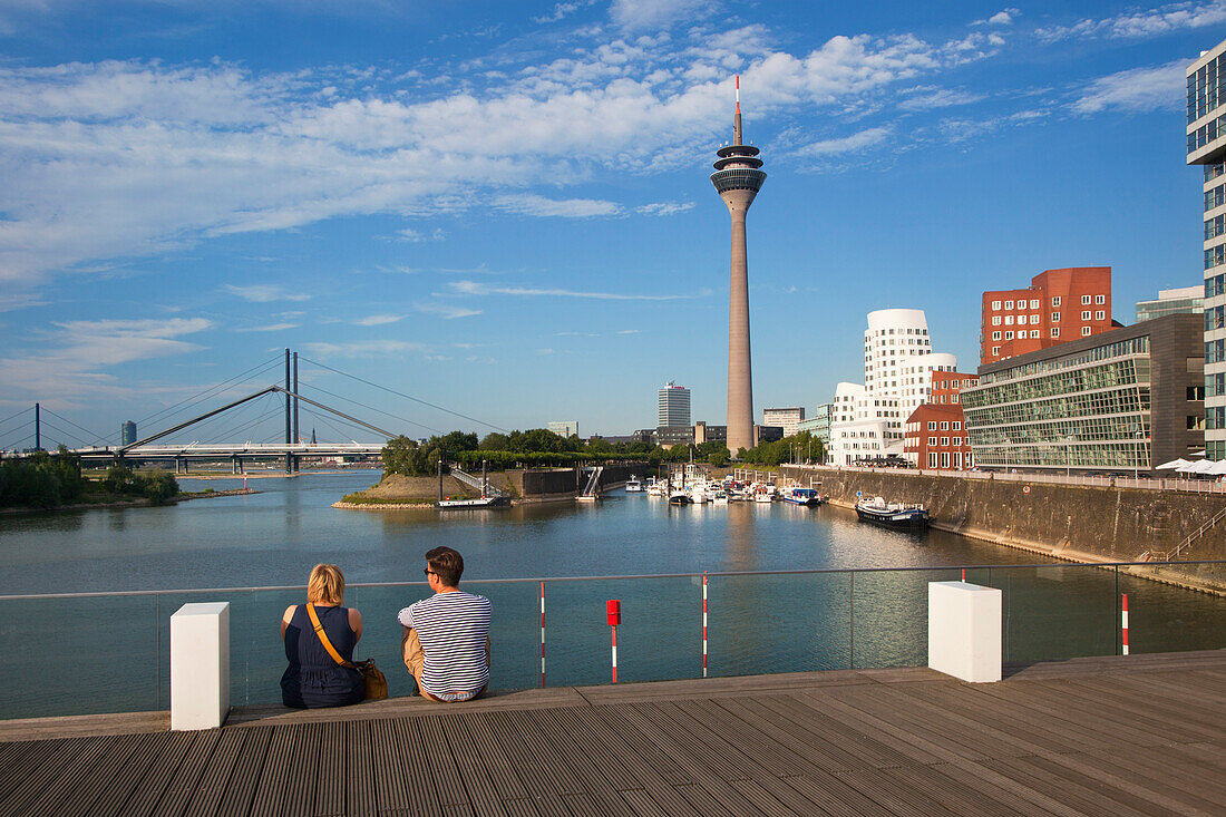 Paar sitzt auf einer Brücke am Medienhafen, Blick auf Rheinturm und Neuen Zollhof, Düsseldorf, Nordrhein-Westfalen, Deutschland, Europa